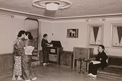 白黒写真。増改築されたと思われるダンスホールの室内を写している。左手では着物姿の女性二人が踊っており、中央にはレコードプレーヤーのような機器を操作する人物がいる。