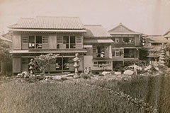 古いセピア調の写真。木造二階建てを中心とした、複数の建物が連なる伝統的な日本建築。瓦屋根、木製の雨戸や障子が見られ、歴史を感じさせる佇まい。